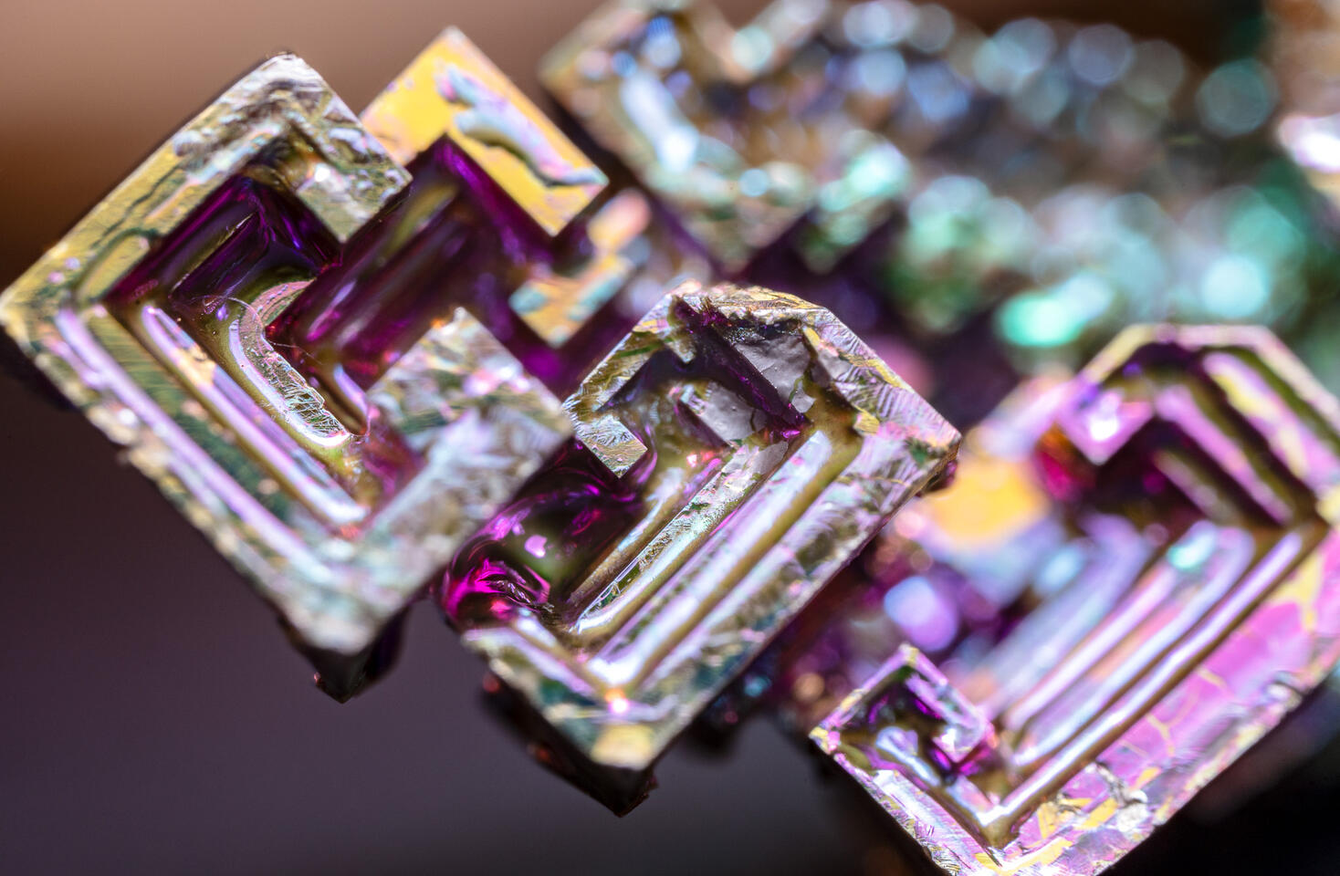 Macro of an iridescent bismuth crystal showing rainbow hues and precise stepped cubic shapes.